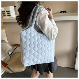 Side view of a large light blue quilted nylon tote bag worn by a model in a cafe