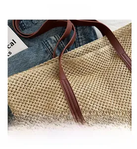 Detail of red-brown leather handles and woven texture on a beige straw tote bag