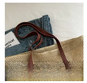 Detail of hand-woven straw tote bag showing brown leather handles and mesh texture