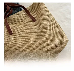 Close-up of straw woven tote bag with premium brown PU leather handles on white linen