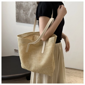 Detail of woven straw tote bag with cream leather straps on female model's shoulder