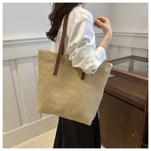 Detail of woven straw tote bag with brown faux leather straps shown on a model