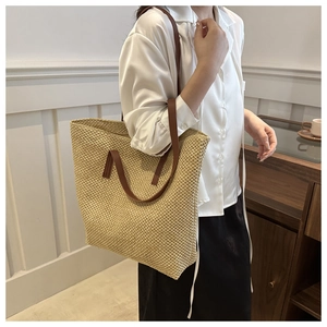 Detail of woven straw tote bag featuring contrast dark brown leather shoulder straps