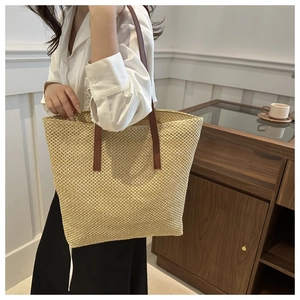 Detail of large woven straw tote bag with brown handles showing material texture