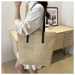 Detailed view of woven straw tote bag with black leather straps on a casual model