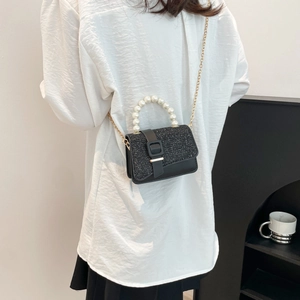 Elegant black leather crossbody bag with pearl handle and glitter flap shown on model