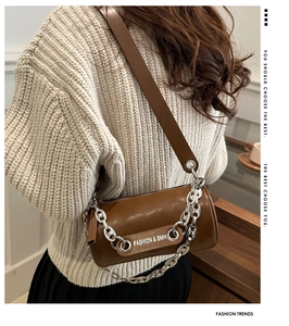 Detail of dark brown cylinder bag with silver metal chain and fashion brand lettering