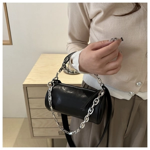 Detail of black cylindrical crossbody bag featuring a thick silver chain handle and strap