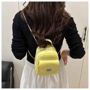 Close-up of bright yellow quilted mini backpack with chain strap on a model's back