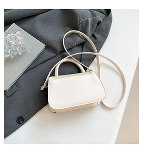 Detail view of a cream crossbody bag with woven texture lid on a modern desk setting