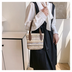 Detail view of colorful striped straw woven tote with dark brown leather handles