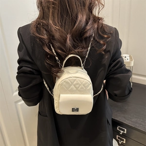 Beige quilted mini backpack with metal lock and chain straps on model's back in black suit