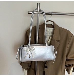 Close-up of silver mirror underarm bag featuring pearl bow and lace heart pendant details