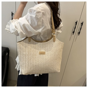 Detail of straw woven tote bag featuring a leather fashion patch and brown shoulder straps