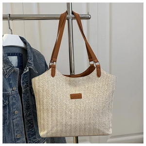 Detail of beige straw tote bag featuring herringbone weave and brown leather strap