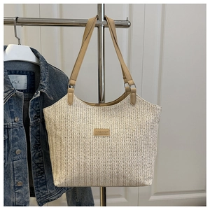 Close-up of beige straw tote bag with V-shaped weave and brown leather fashion patch