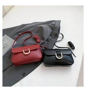 Detail view of red and black leather crossbody bags with golden U-shaped metal buckles