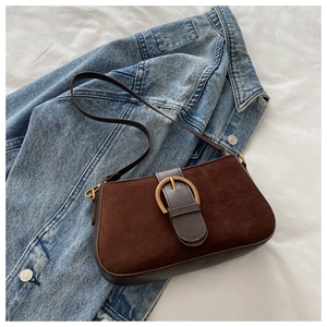 Détail d'un sac bandoulière vintage en daim marron avec boucle dorée sur tissu blanc