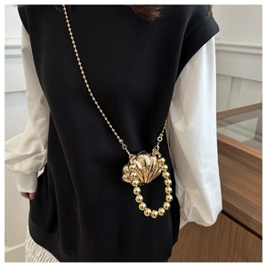 Macro shot of stylish gold shell-shaped mini bag with elegant pearl chain and metallic texture