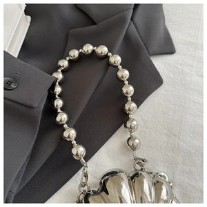 Detail of silver metallic heart shell bag with beaded strap on a grey blazer background