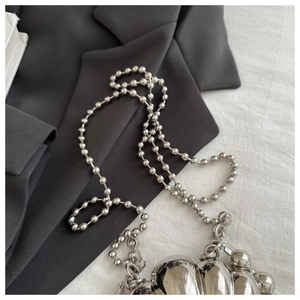 Close-up of metallic silver shell bag with ball chain strap on grey fabric