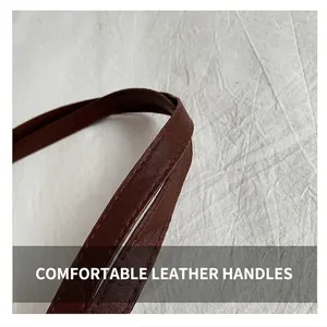 Detailed close-up of dark brown leather handbag handle with fine stitching and lychee grain