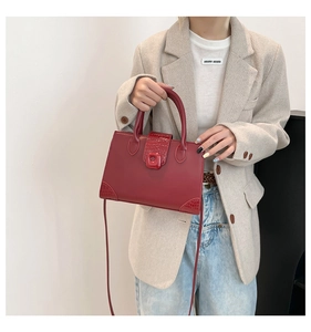 Dettaglio borsa rossa con trama a coccodrillo e fibbia su blazer beige