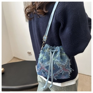 Dettaglio di una borsa a secchiello in denim blu con stelle e bordi sfrangiati indossata