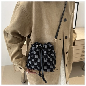 Dettaglio borsa a secchiello in denim a scacchi con bordi sfrangiati e hardware dorato