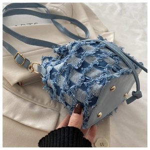 Dettaglio della base della borsa a secchiello in denim blu con rivetti dorati di lusso