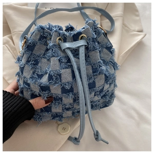 Dettaglio della borsa a secchiello in denim a scacchi con bordi sfrangiati e coulisse
