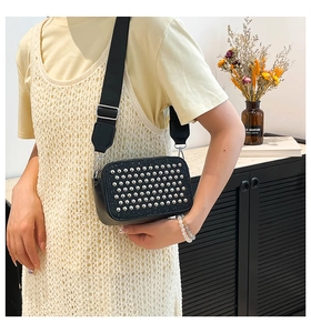 Detail of black crossbody camera bag with silver rivets and wide strap shown on model