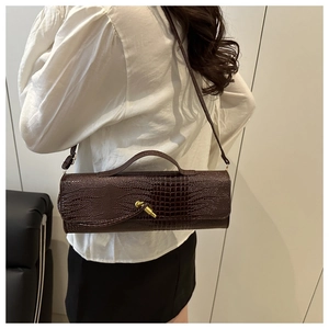 Detail showing dark brown crocodile embossed barrel bag with gold hardware and shoulder strap