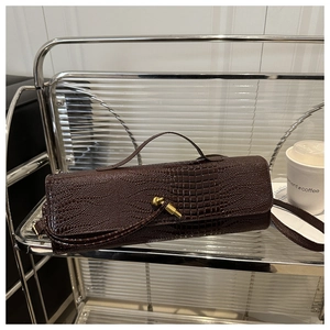 Détail d'un sac à main marron foncé à motif crocodile avec boucle dorée sur étagère métal
