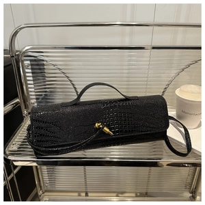Détail du sac cylindrique noir motif crocodile avec fermoir nœud doré sur étagère