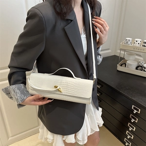 Sac à main blanc à motif crocodile avec fermoir nœud doré porté par un mannequin