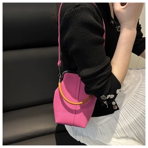 Rose pink handbag with wooden handle shown on a model against a black leather background