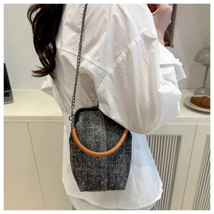 Detail of tweed crossbody bag with metal chain strap and round handle worn by model