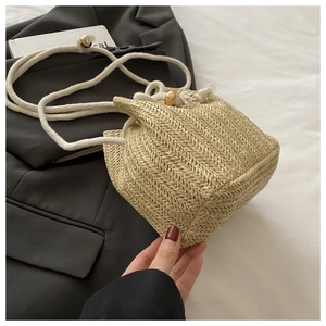 Detail of straw woven bucket bag with V-shaped texture and white rope strap for beach style