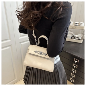Detail of minimalist cream leather handbag featuring a sleek silver metal bar buckle closure