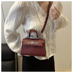 Detail view of burgundy textured leather kelly bag with silver buckle worn cross-body