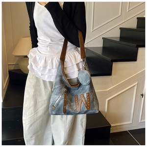 Detalle de bolso tote denim azul con asas de cuero y parche decorativo de letra W