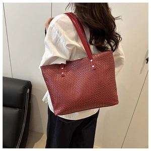 Detail of red woven tote bag featuring silver rivets and wide shoulder strap style