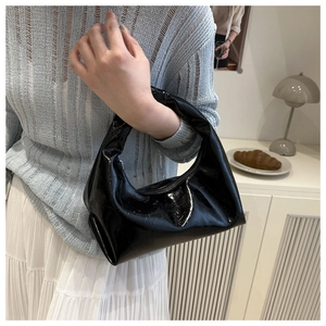 Close-up of black glossy crescent bag with wrinkled texture styled in a chic outfit