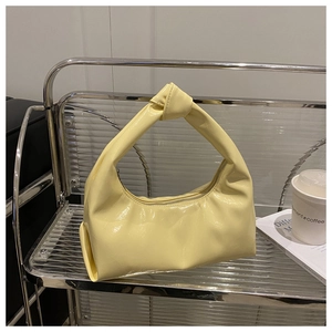 Detail of light yellow patent leather handbag with a knotted handle on a stylish shelf
