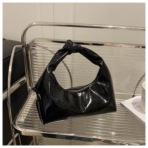 Detail of glossy black patent leather crescent bag featuring a knotted handle and silver zipper
