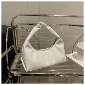 Detail of white crescent bag with unique knotted handle and glossy patent leather finish