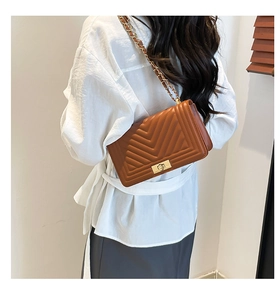 Close-up of brown quilted shoulder bag with V-pattern and gold chain strap on model