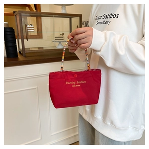 Close-up of red canvas handbag with golden embroidery and colorful beaded handle