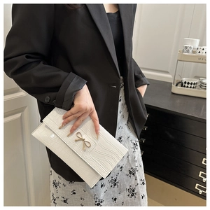 Close-up of white croc-embossed envelope clutch bag with gold bow decoration